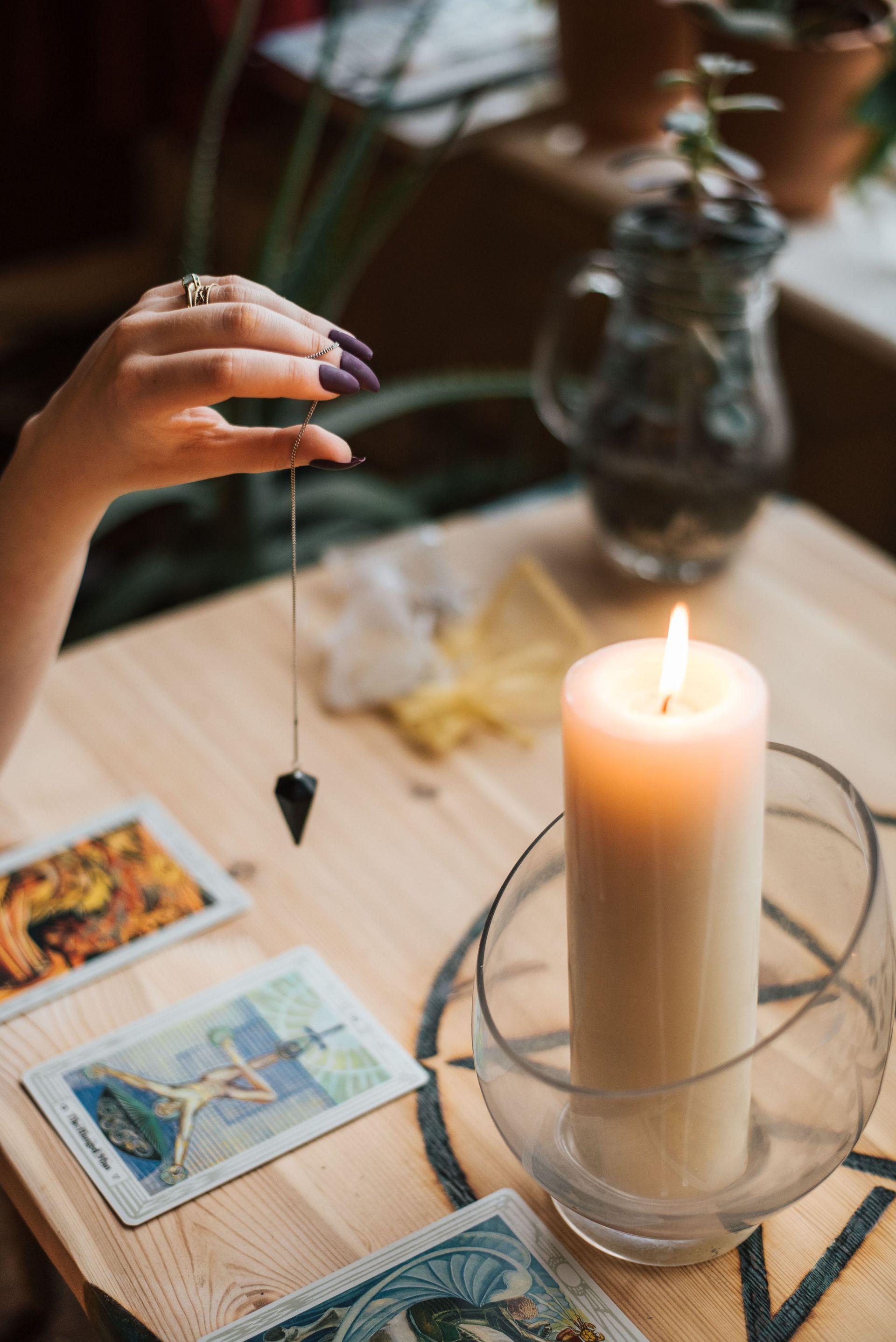 From above of crop anonymous female fortune teller with amulet on thread above tarot cards near burning candle on table